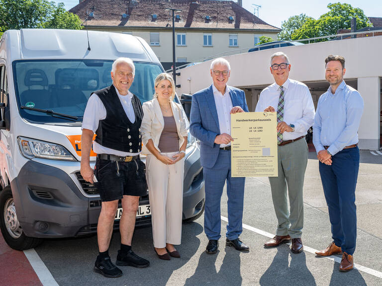 Fünf Personen stehen neben einem Transporter und halten ein großes Dokument, während sie in die Kamera lächeln.