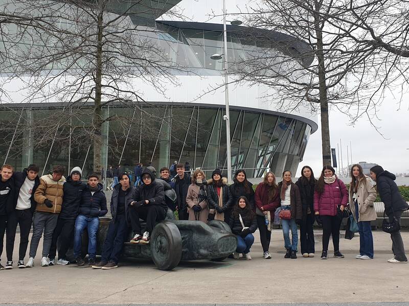 Eine Gruppe von Menschen posiert vor einem modernen Gebäude mit Glasfassade, umgeben von kahlen Bäumen.