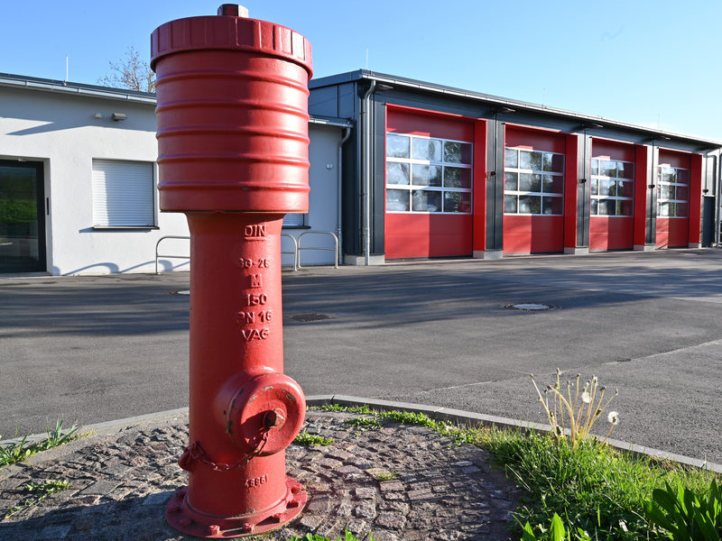 Ein roter Hydrant steht auf einer Pflasterfläche vor einem Gebäude mit mehreren geschlossenen roten Toren.