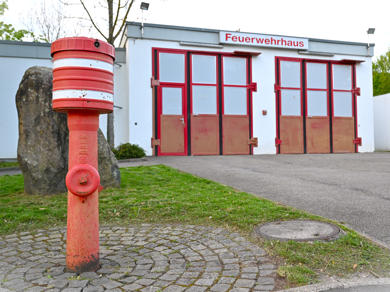 Ein roter Hydrant steht vor einem Gebäude mit roten Toren und einem Schild mit der Aufschrift "Feuerwehrhaus".