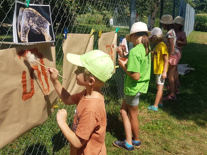 Eine Gruppe von Kindern malt im Freien auf an einem Zaun befestigtes Papier.