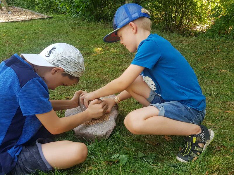 Zwei Jungen sitzen auf dem Rasen und bearbeiten gemeinsam einen Stein in einem Garten.