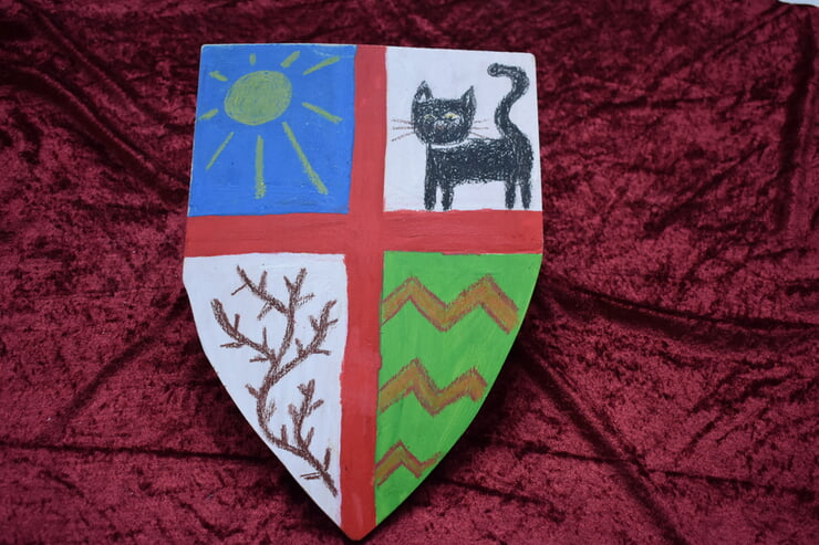 Ein in vier Abschnitte unterteiltes Wappen zeigt oben links eine Sonne, oben rechts eine schwarze Katze, unten links einen kahlen Zweig und unten rechts grüne und braune Zickzacklinien.