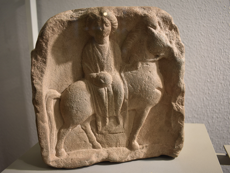 Eine alte Steinreliefskulptur zeigt eine sitzende Figur auf einem Pferd.