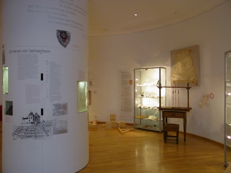 Ausstellung des Museums, links ist eine Infotafel zu sehen, rechts Schaukästen mit Ausstellungsobjekten