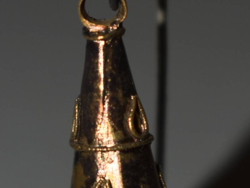 Ein römischer Goldohrring / Ein kleines, goldenes, konisches Metallobjekt mit dekorativen Tröpfchenmuster hängt an einem dünnen Metallhaken.