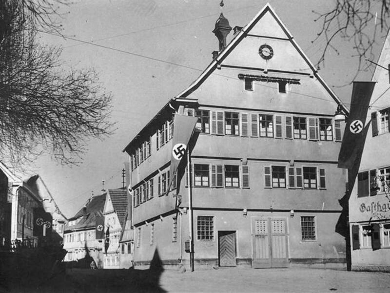 Ein historisches Gebäude mit mehreren Fenstern ist mit großen Hakenkreuzflaggen bestückt.
