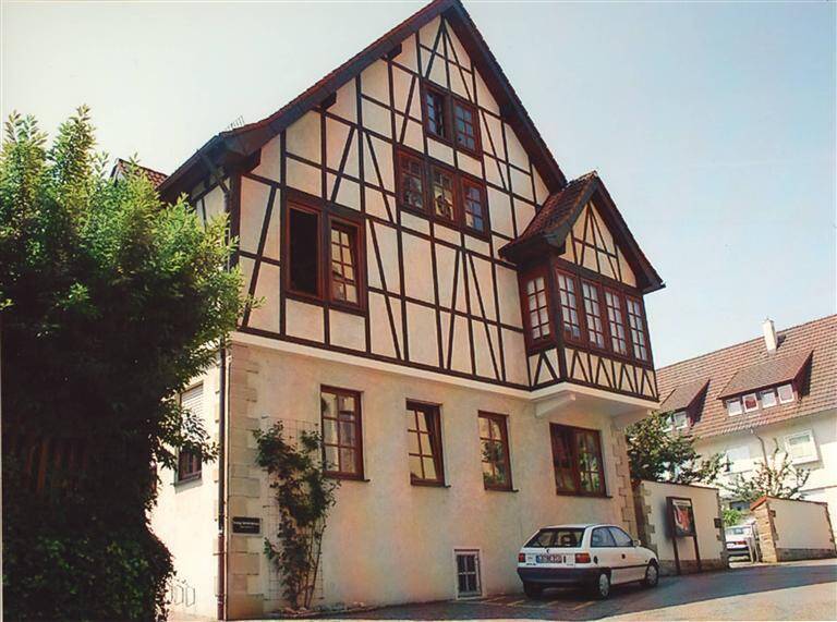 Ein zweistöckiges Fachwerkhaus mit schrägem Dach und mehreren Fenstern, vor dem ein Auto geparkt ist.