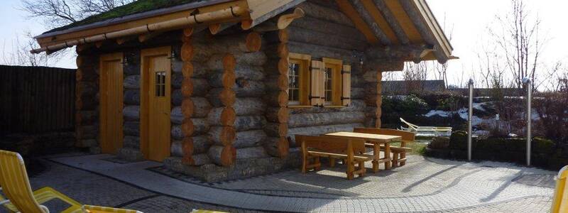 Das Bild zeigt ein Holzhaus von der Seite, im Vordergrund stehen gelbe Liegestühle.