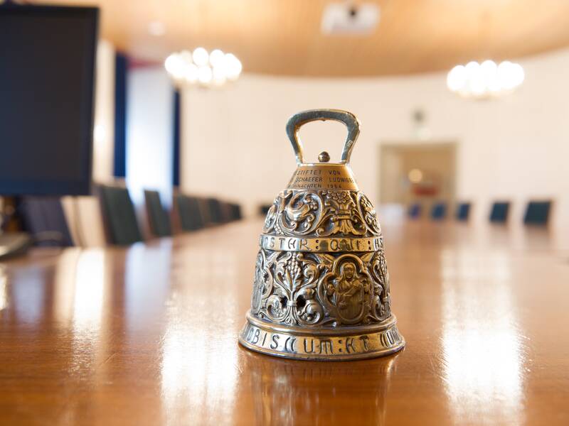 Eine verzierte Glocke steht auf einem langen Konferenztisch in einem Sitzungssaal.