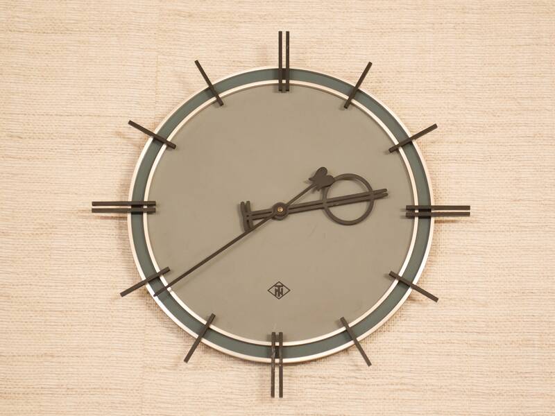 Eine stilvolle Wanduhr mit einem hellgrauen Zifferblatt und minimalistischen schwarzen Stundenmarkierungen hängt an einer beigen Wand.