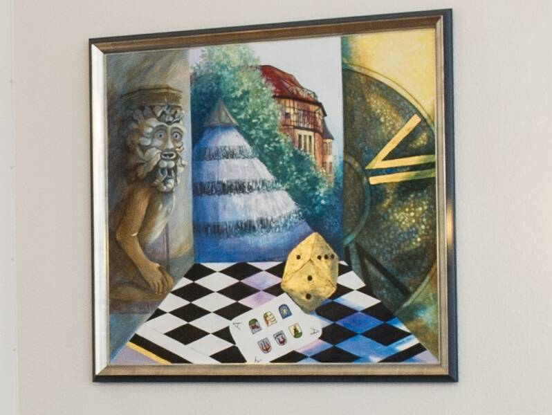 Das Bild zeigt einen surrealistischen Mix aus einem Löwenrelief, geometrischen Formen wie einem Würfel und Schachbrettmuster, sowie einem Gebäude im Hintergrund.