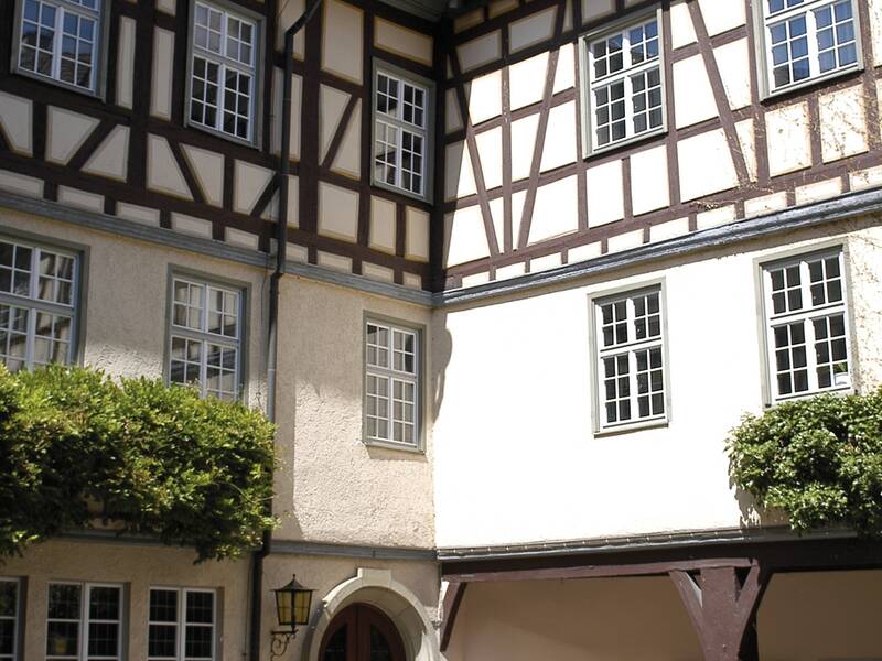 Ein Innenhof mit einer Fachwerkfassade, einem Eingang mit rundem Bogen und Blumenkästen an den Fenstern.
