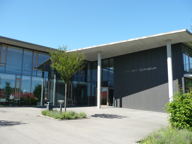 Ein modernes Schulgebäude mit großen Glasfenstern und der Aufschrift "Lichtenstern-Gymnasium" an der Fassade, umgeben von Bäumen und Pflanzen.