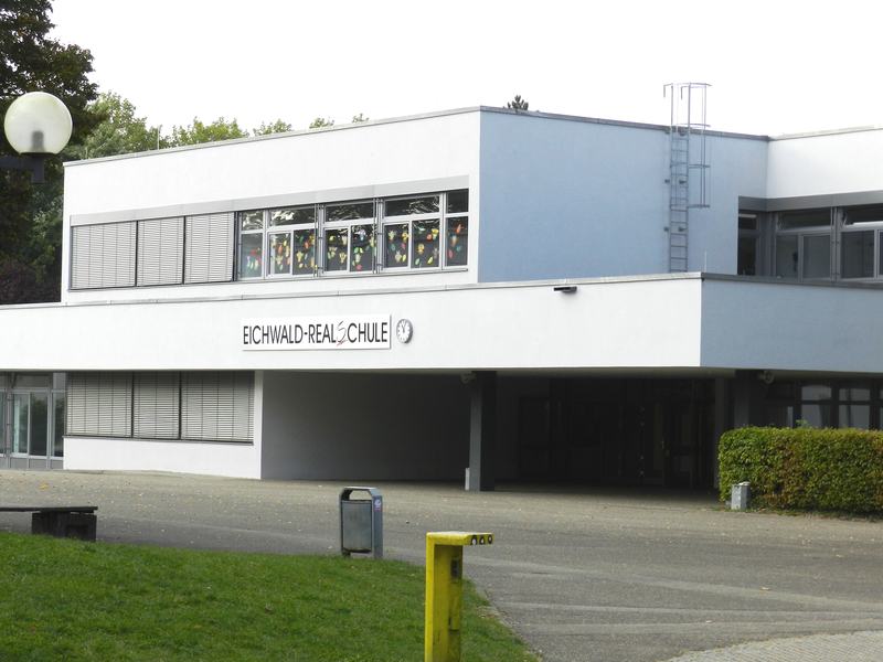 Ein modernes zweistöckiges Schulgebäude mit der Aufschrift "Eichwald-Realschule" und großen Fenstern, umgeben von Grünflächen.
