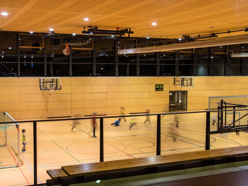 Eine Turnhalle mit Holzwänden, in der mehrere Personen ein Spiel spielen, umgeben von Basketballkörben und Fußballtoren.