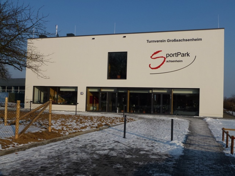 Ein modernes Gebäude mit der Aufschrift "Turnverein Großsachsenheim SportPark Sachsenheim" steht in einer verschneiten Umgebung.
