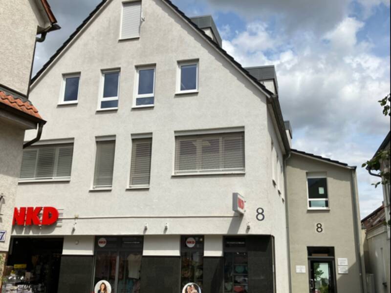 Ein Gebäude mit einem Geschäft im Erdgeschoss mit der Aufschrift "NKD" und mehreren Fenstern sowie Hausnummer "8" unter einem bewölkten Himmel.