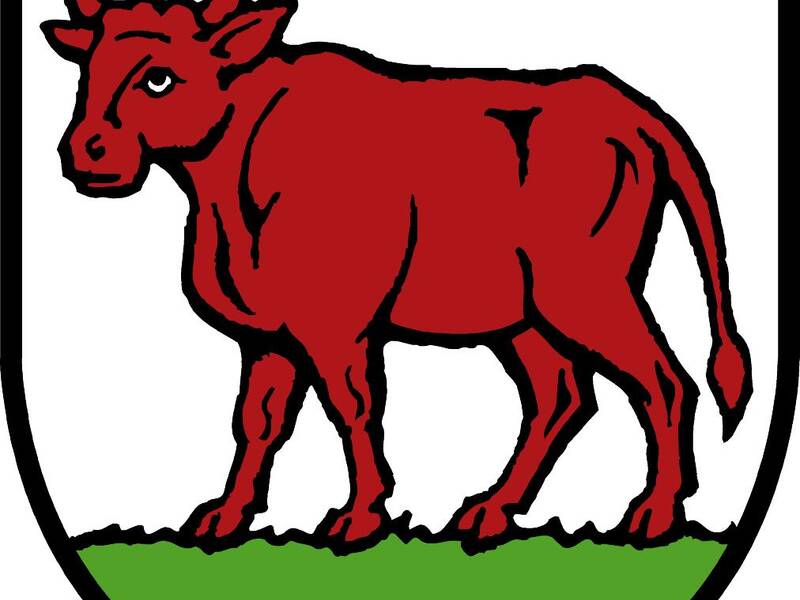 Ein roter Stier steht auf grünem Boden innerhalb eines Schildes mit schwarzem Rand.