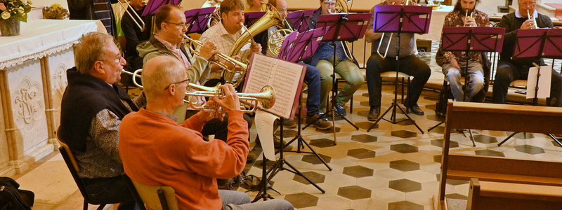 Das Bild zeigt eine Personengruppe die Musikinstrumente in einem Kirchenraum spielen.