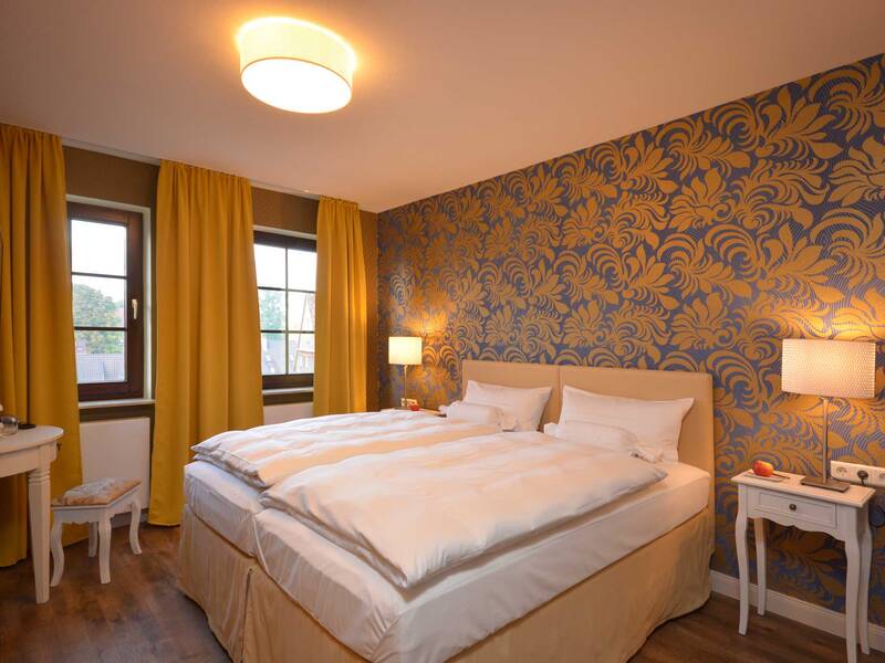 Ein gemütliches Schlafzimmer mit einem großen Bett, gelben Vorhängen und einer dekorativen Blumenmuster-Tapete an der Wand.