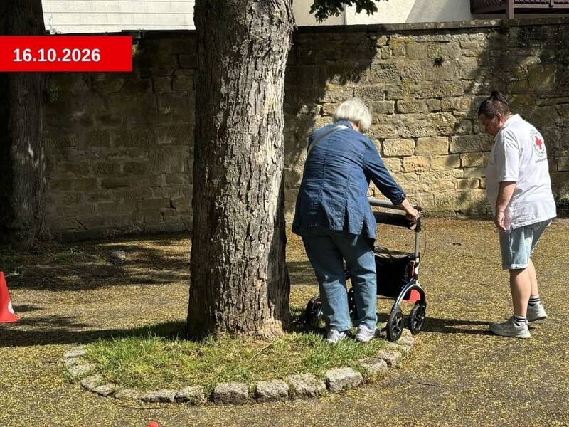 Eine ältere Person absolviert mit Unterstützung einer anderen Person ein Rollatortraining im Freien.