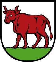 Ein roter Stier steht auf grünem Boden innerhalb eines Schildes mit schwarzem Rand.