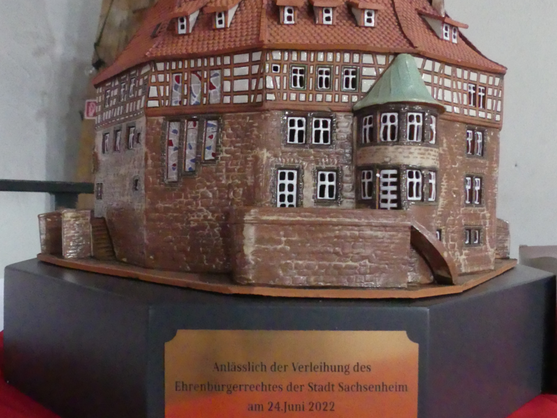 Ein Miniaturmodell eines Fachwerkgebäudes steht auf einem Sockel mit einer goldfarbenen Plakette, die anlässlich der Verleihung des Ehrenbürgerrechtes der Stadt Sachsenheim am 24. Juni 2022 angebracht wurde.