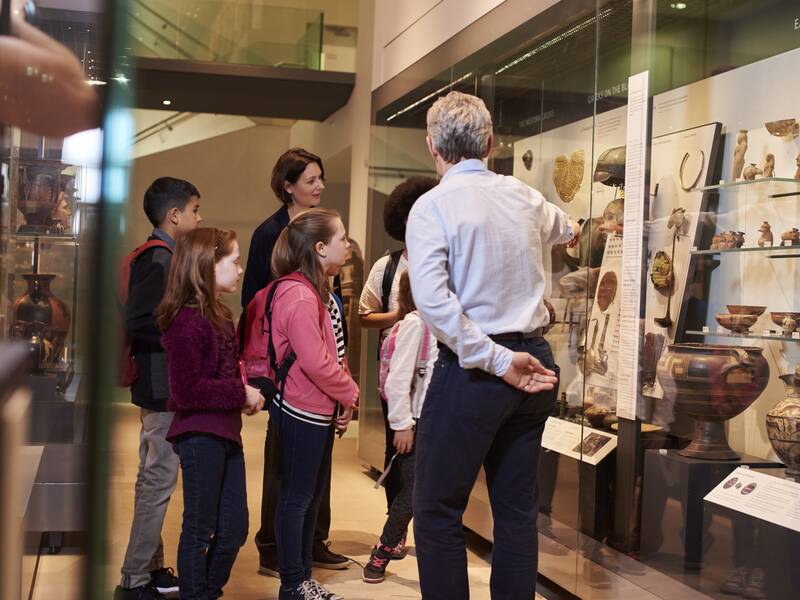 Eine Führung durch ein Museum, zwei erwachsene erklären Kindern was sie im Schaukasten sehen