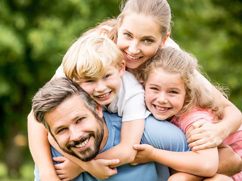 Eine fröhliche Familie, bestehend aus zwei Erwachsenen und zwei Kindern, posiert glücklich aufeinander gestapelt vor einem grünen Hintergrund.