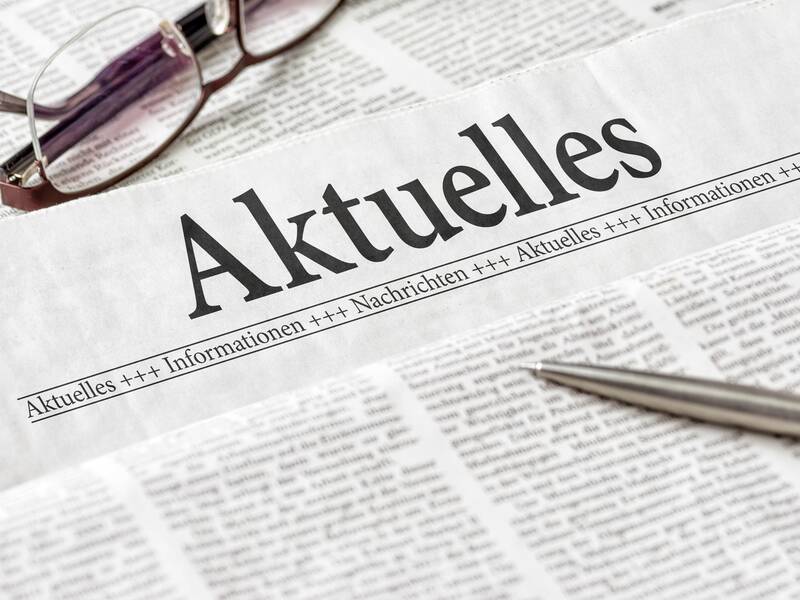 Eine Zeitung mit dem Titel "Aktuelles" und daneben eine Brille sowie ein Stift.