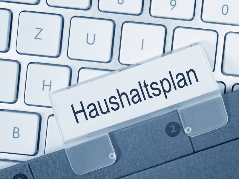Eine weiße Computertastatur, über der eine Datei mit dem Etikett "Haushaltsplan" liegt.