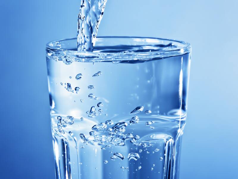 Ein Glas wird mit klarem Wasser gefüllt, wobei Luftblasen aufsteigen.