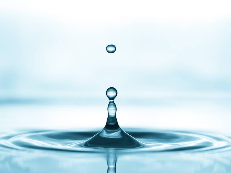 Ein Wassertropfen fällt in eine Wasseroberfläche und verursacht konzentrische Wellen.
