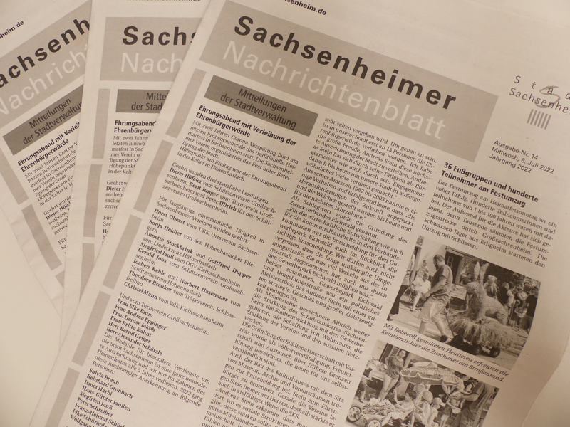 Das Bild zeigt mehrere überlappende Ausgaben des "Sachsenheimer Nachrichtenblatts" mit verschiedenen Artikeln und Fotos auf der Titelseite.