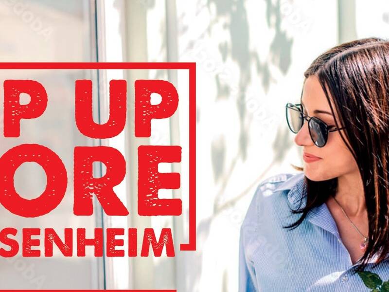 Eine Person mit Sonnenbrille steht neben einem großen roten Schild mit der Aufschrift "Pop Up Store Sachsenheim".