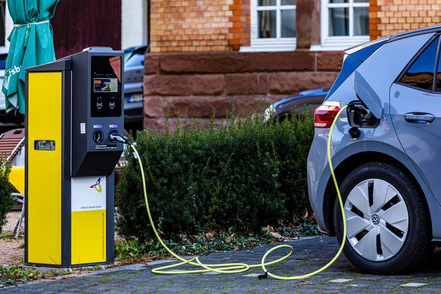 Eine gelb-graue E-Ladestation für Elektroautos. Von der Ladestation führt ein Ladekabel in die Tanköffnung eines grauen Autos.
